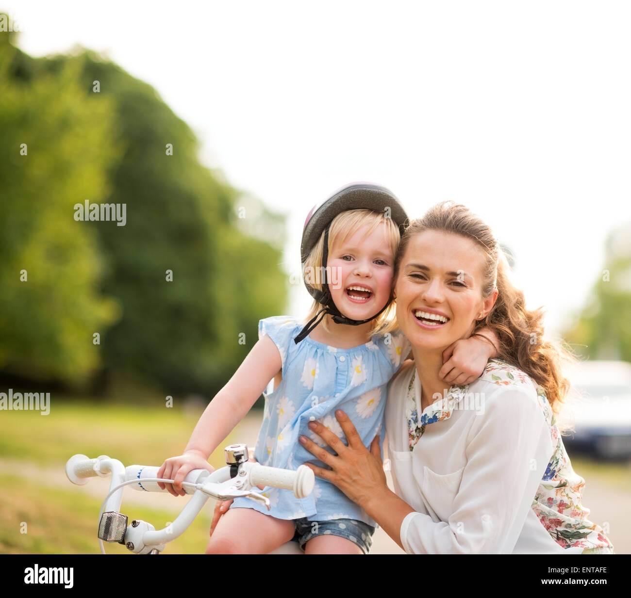 Stolzer Moment zwischen einer Mutter und einer Tochter, die gerade ihr Fahrrad fahren gelernt, hat geteilt. Die Mutter kniet liebevoll ihre Tochter hielt sie sanft, wie ihre Tochter einen liebevolleren Arm um ihre Mutter Hals wirft. Beide sind lächelnd, glücklich und stolz. Stockfoto