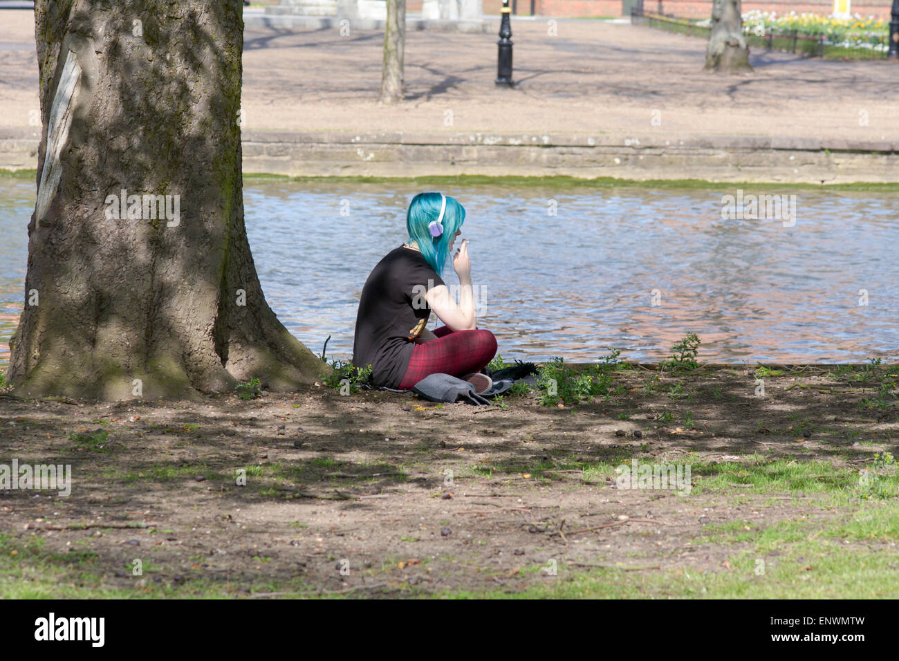 Frau mit grünen Haaren Raucher sitzen unter Baum neben dem Fluss Ouse in Bedford, Bedfordshire, England Stockfoto