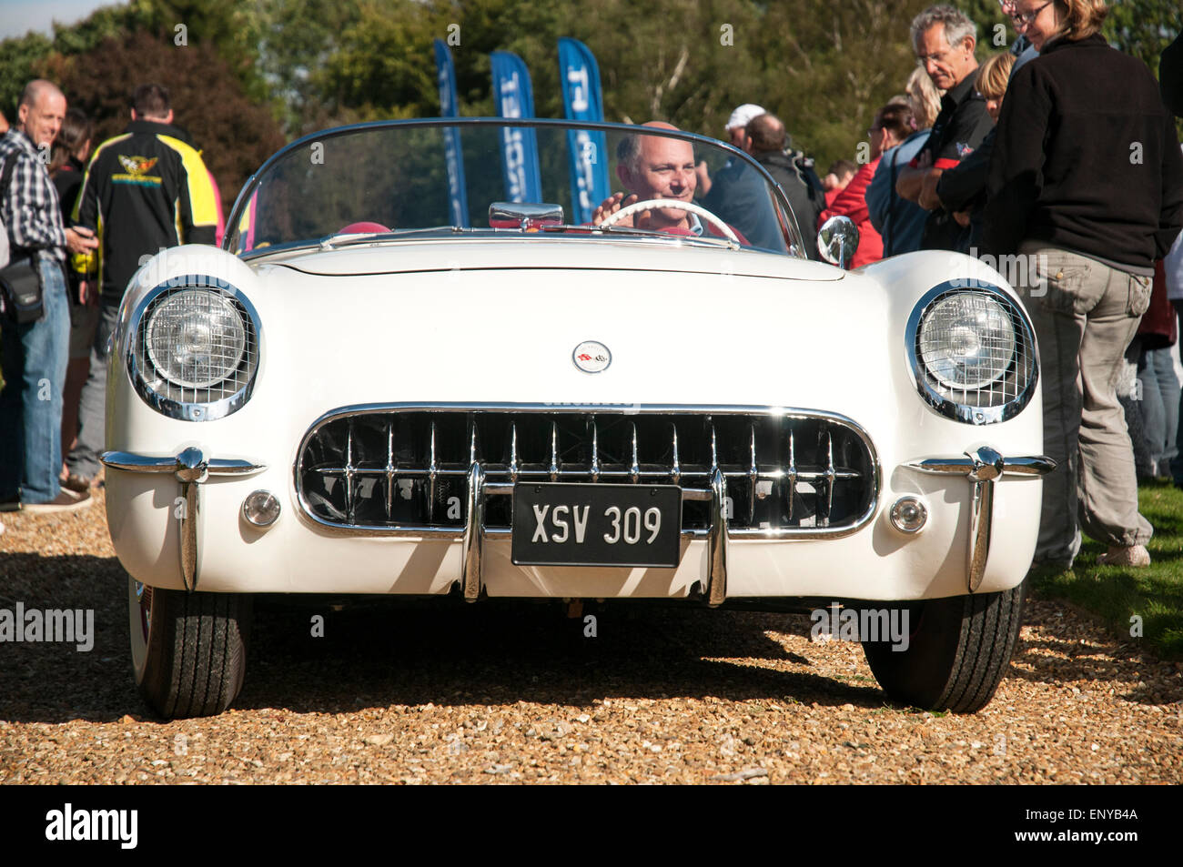 Front-End-Blick auf eine weiße, klassische amerikanische Korvette Sportwagen auf einem Kiesweg mit Fahrer und mehrere auf Zuschauer in der Nähe. Stockfoto