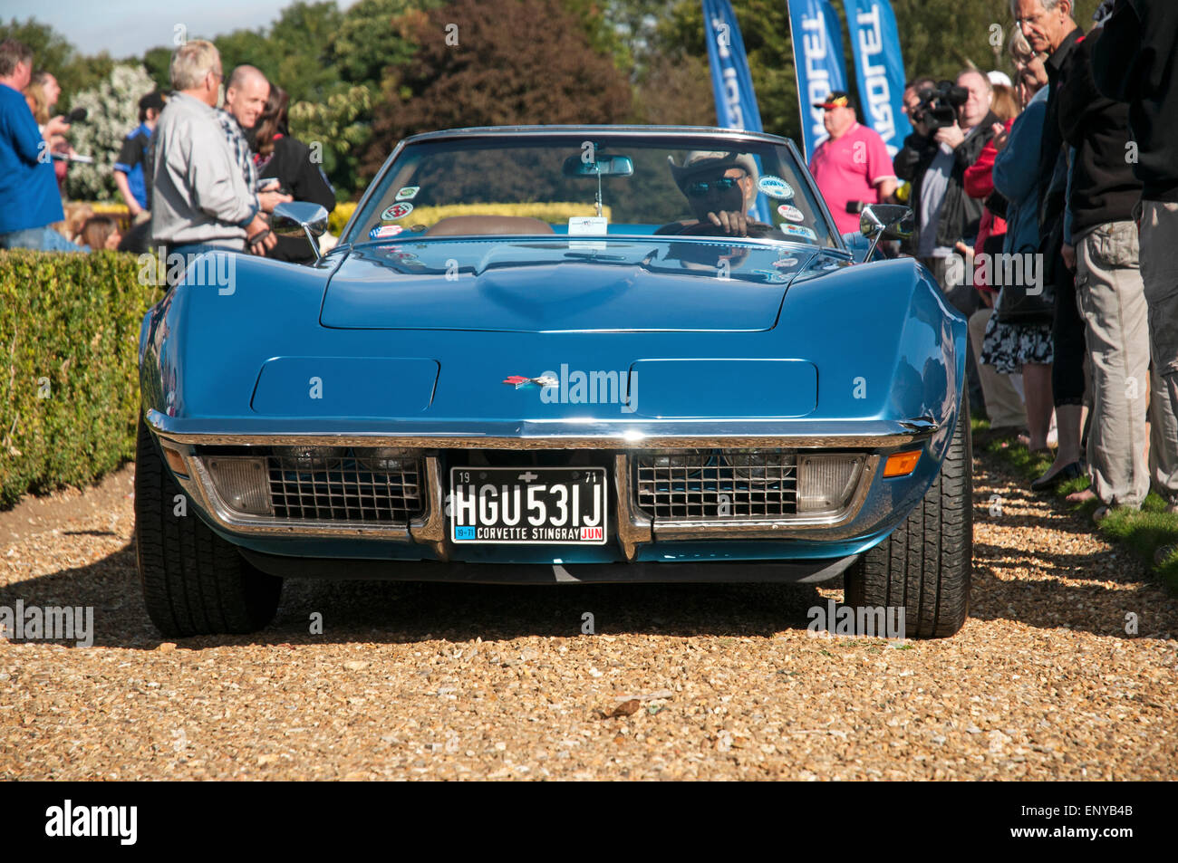 Front-End-Blick auf eine blaue, klassische amerikanische Korvette Sportwagen auf einem Kiesweg mit Fahrer und mehrere auf Zuschauer in der Nähe. Stockfoto