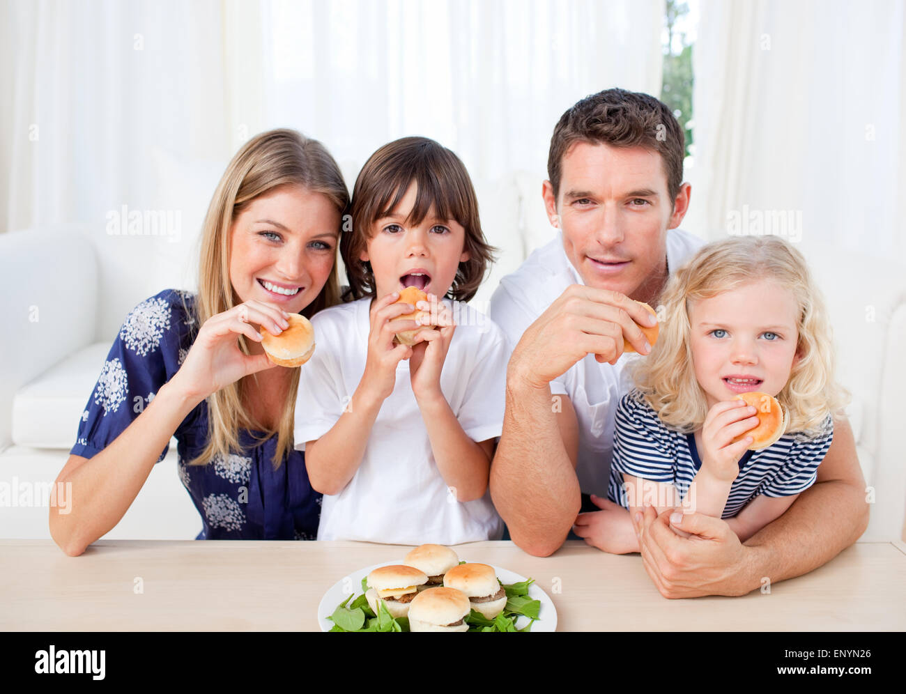 Begeisterte Familie essen Burger im Wohnzimmer Stockfoto