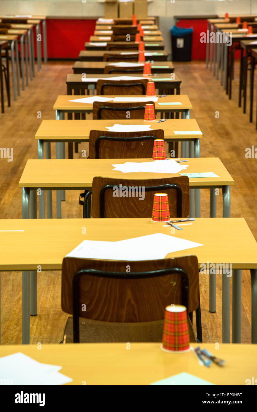 Reihen von Tischen und Stühlen mit Papier und Pokale warten auf die Prüfung am Gymnasium Stockfoto