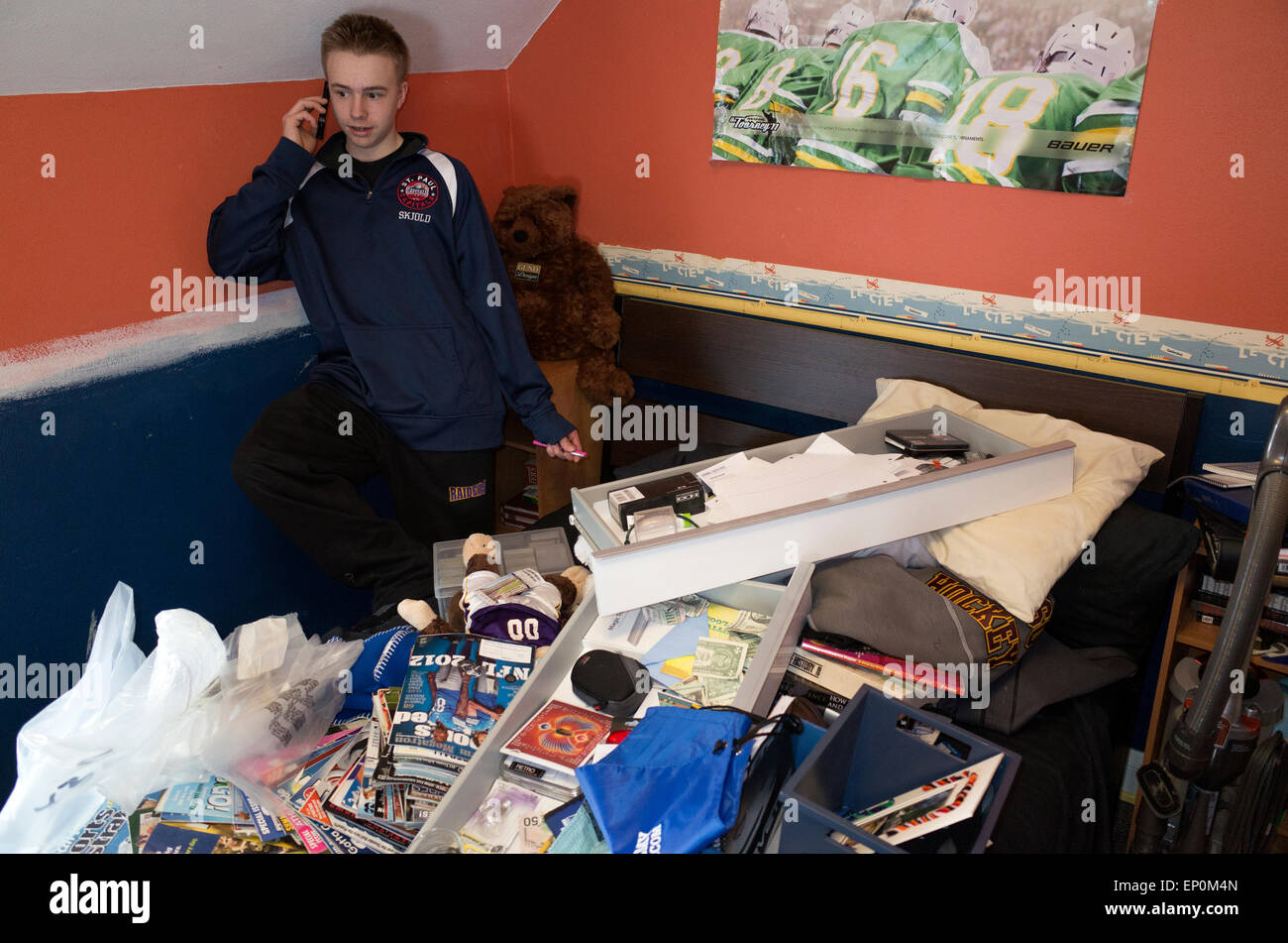 Männliche Teenager nimmt sich eine Auszeit auf Handy zu sprechen, während er seinem Schlafzimmer reinigt.  St Paul Minnesota MN USA Stockfoto