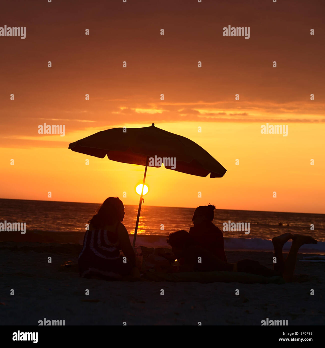 Menschen sitzen und liegen unter dem Sonnenschirm am Sandstrand Cavancha bei Sonnenuntergang in Iquique, Chile Stockfoto