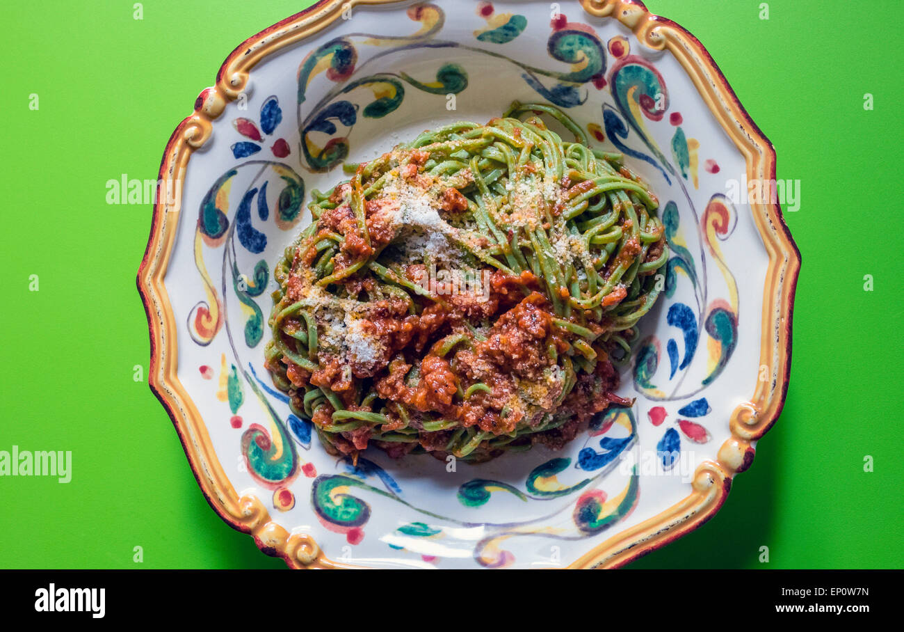 Spinat Nudeln Bolognese in einer reich verzierten Pastaschüssel am grünen Tisch Stockfoto