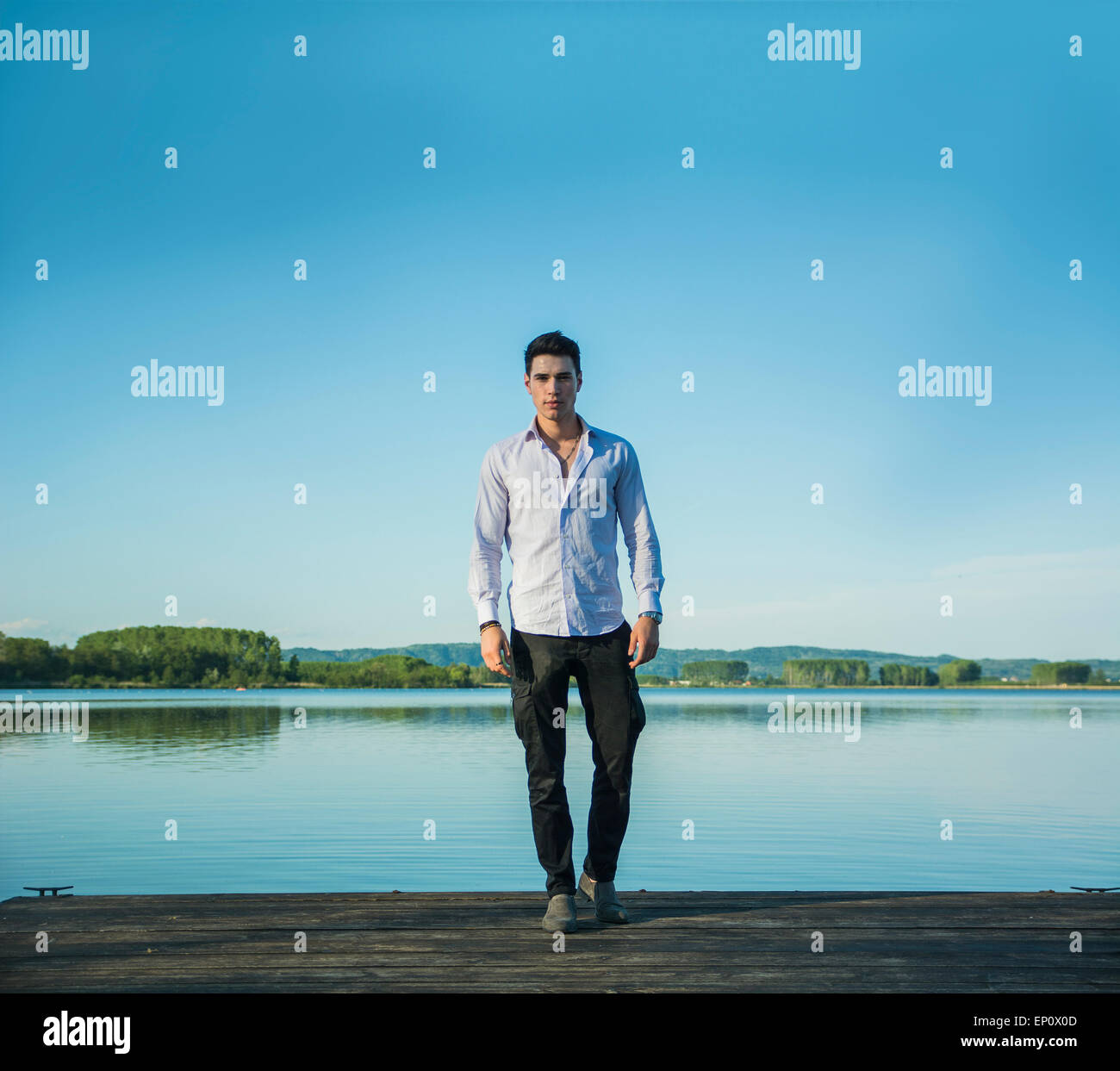 Hübscher junger Mann an einem See an einem sonnigen, ruhigen Tag, stehend auf einem hölzernen pier Stockfoto