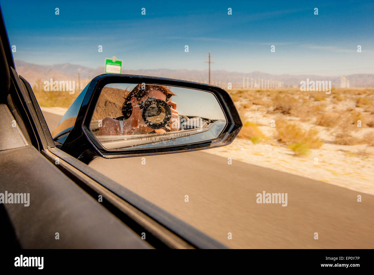 Junge Frau mit einer Kamera sieht man im Rückspiegel auf ein Auto in der Nähe von Palm Springs, Kalifornien Stockfoto