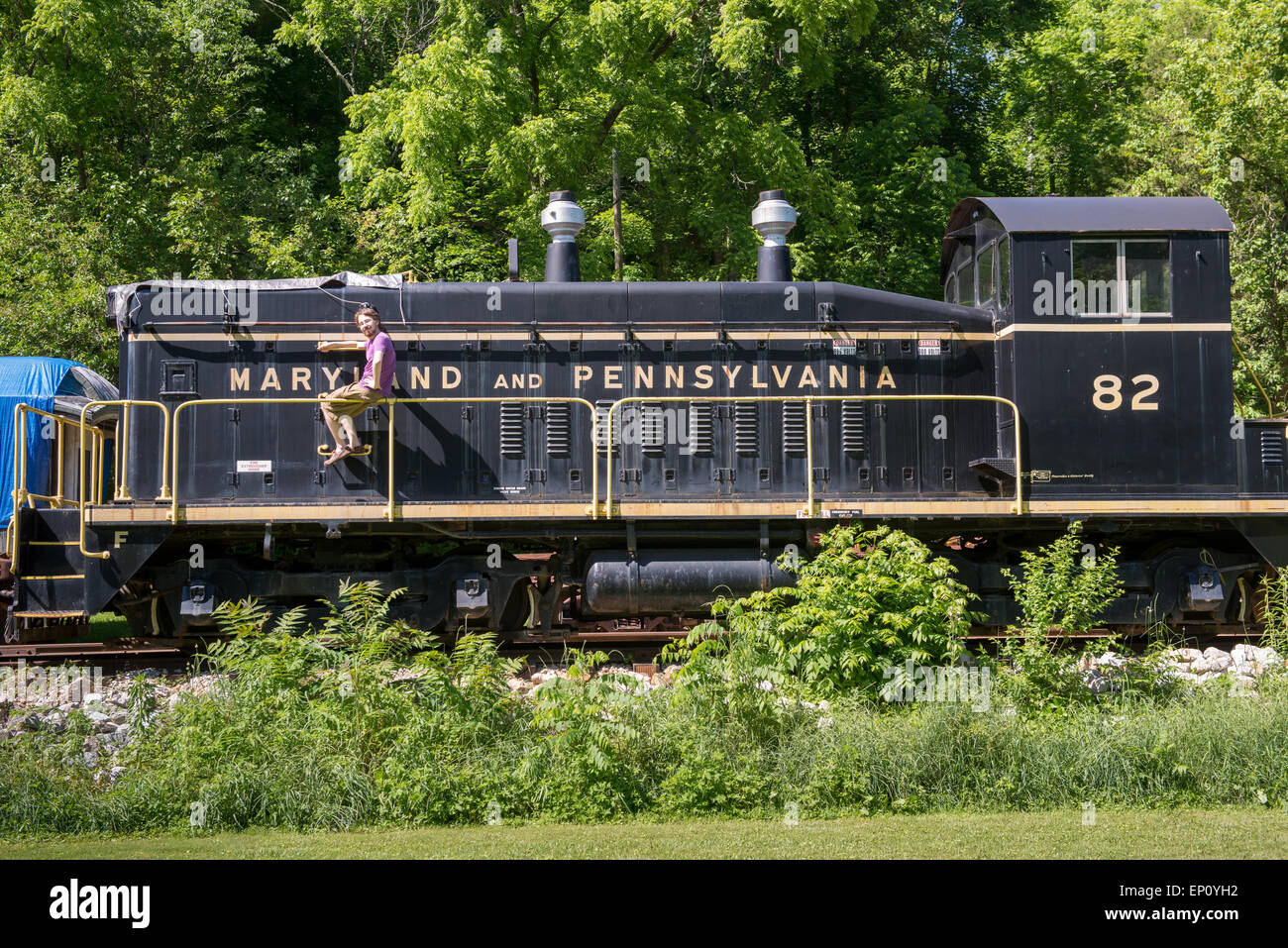 Junger Mann sitzt auf Geländer neben historischen Zug in Muddy Creek Gabeln, Pennsylvania, USA Stockfoto