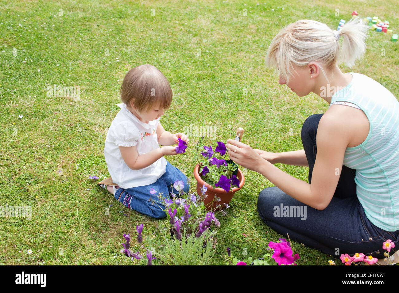 Blonde Mutter zeigt ihrer Tochter eine lila Blume Stockfoto
