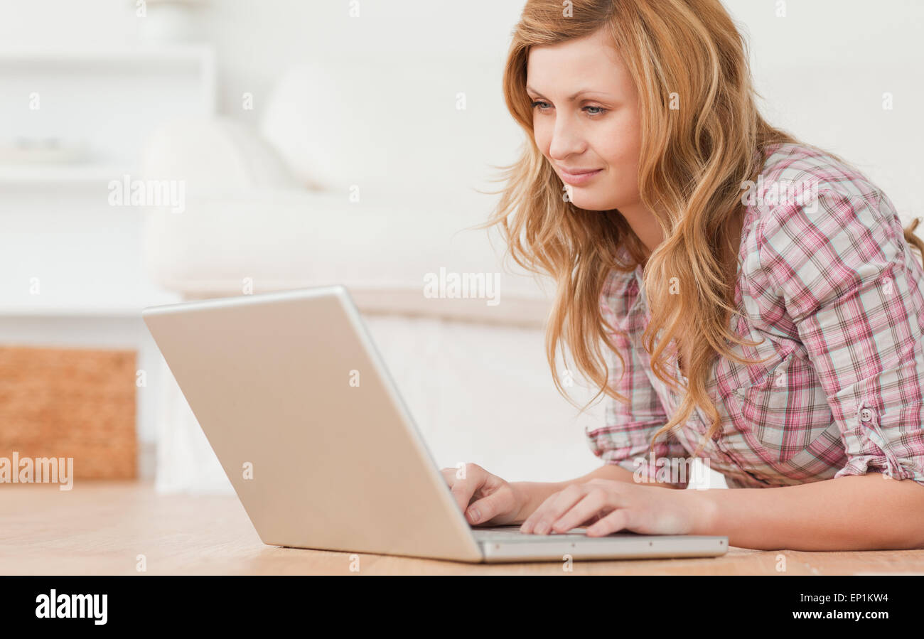 Blonde Frau, die arbeitet auf ihrem Laptop auf dem Boden liegend Stockfoto