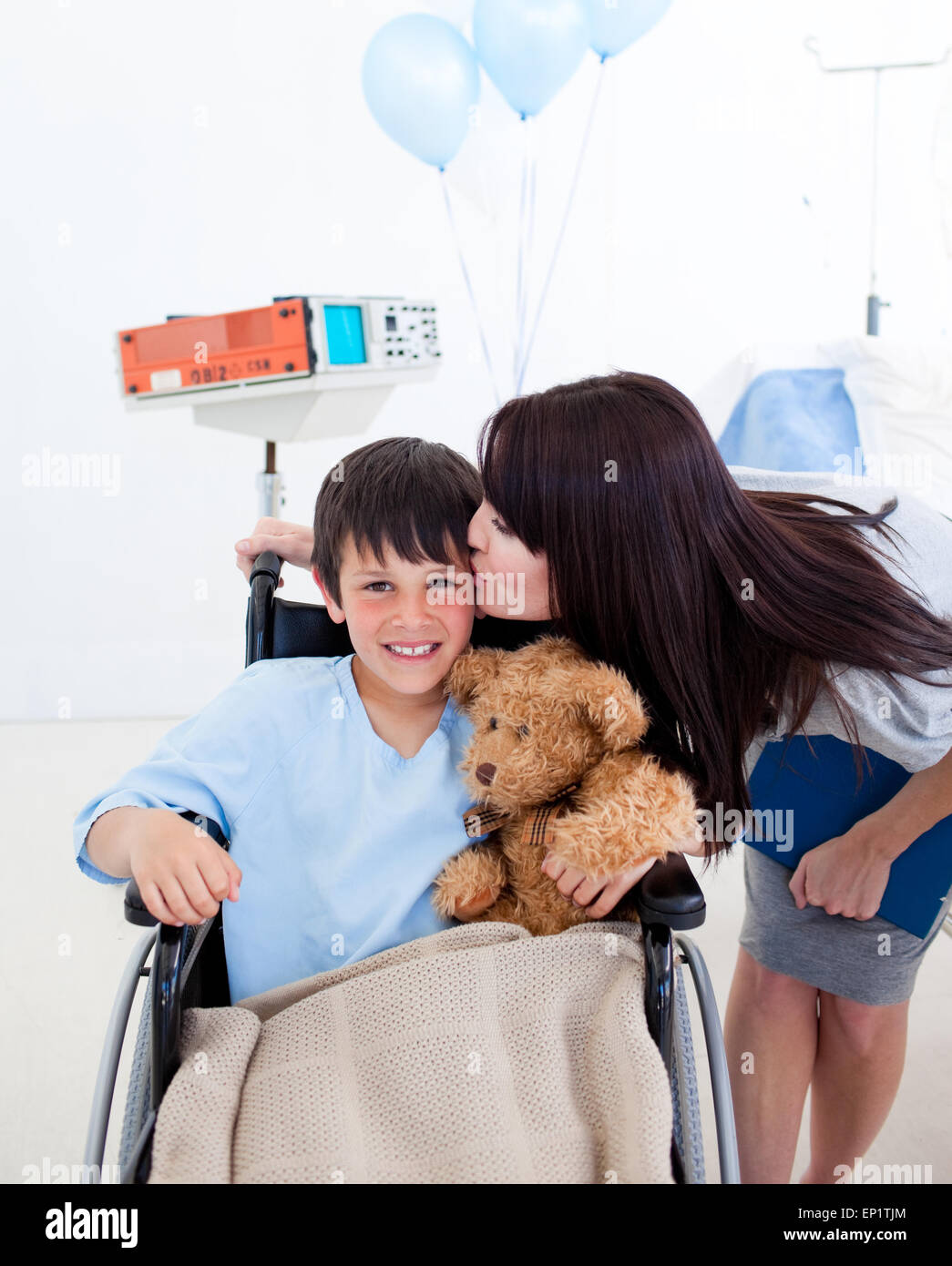 Fröhlicher kleiner Junge sitzt im Rollstuhl und seine Mutter Stockfoto