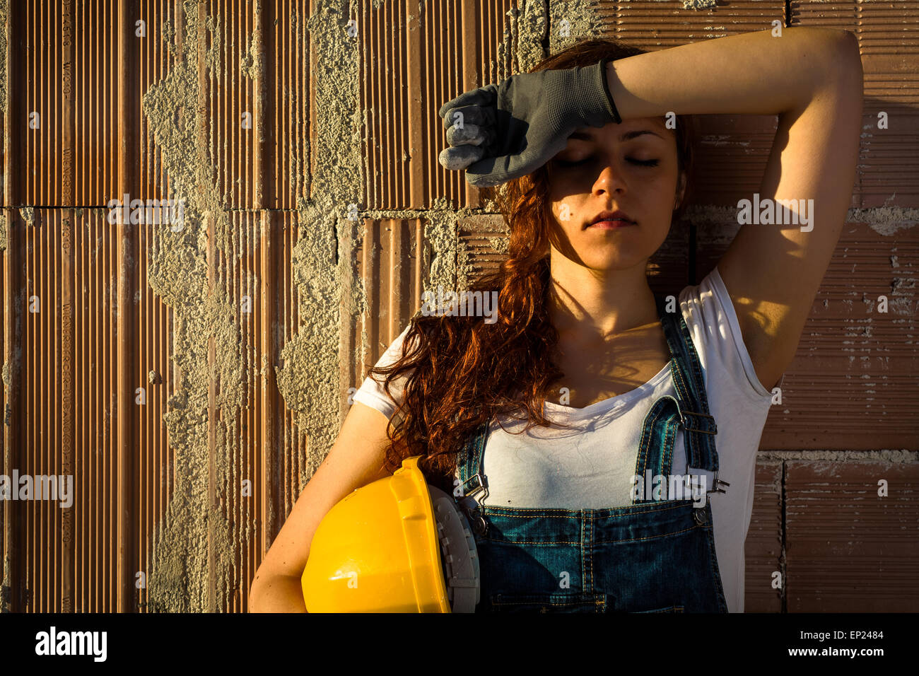 Müde Frau Maurer mit Overall und Helm steht man vor einer Mauer Stockfoto