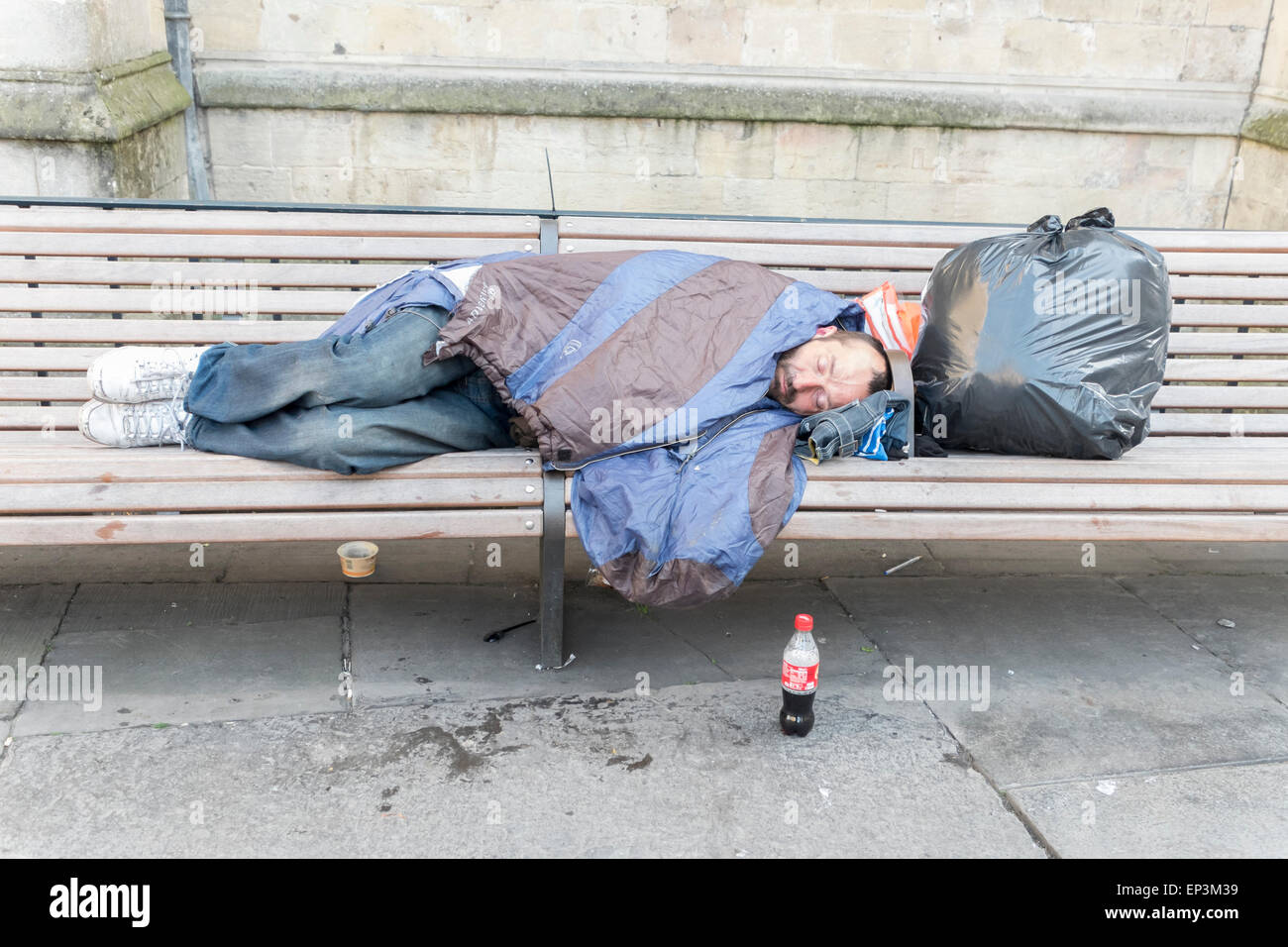 Eine Obdachlosigkeit Person schlafen rau auf einer Bank im Bad Somerset mit einer Tasche von Gegenständen Stockfoto