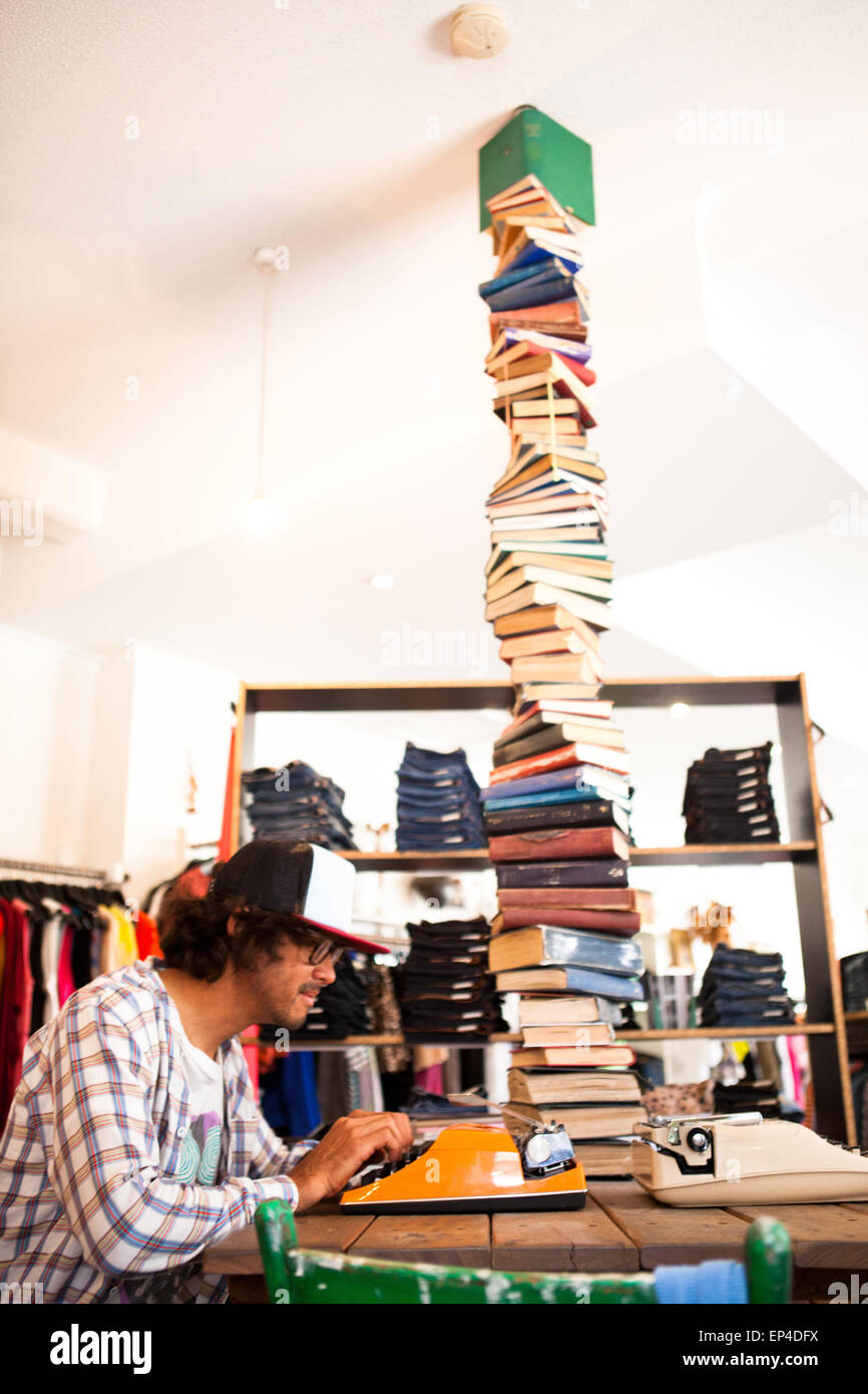 Ein Mann sitzt auf seinem orange Schreibmaschine mit einem Stapel Bücher neben ihm. Stockfoto