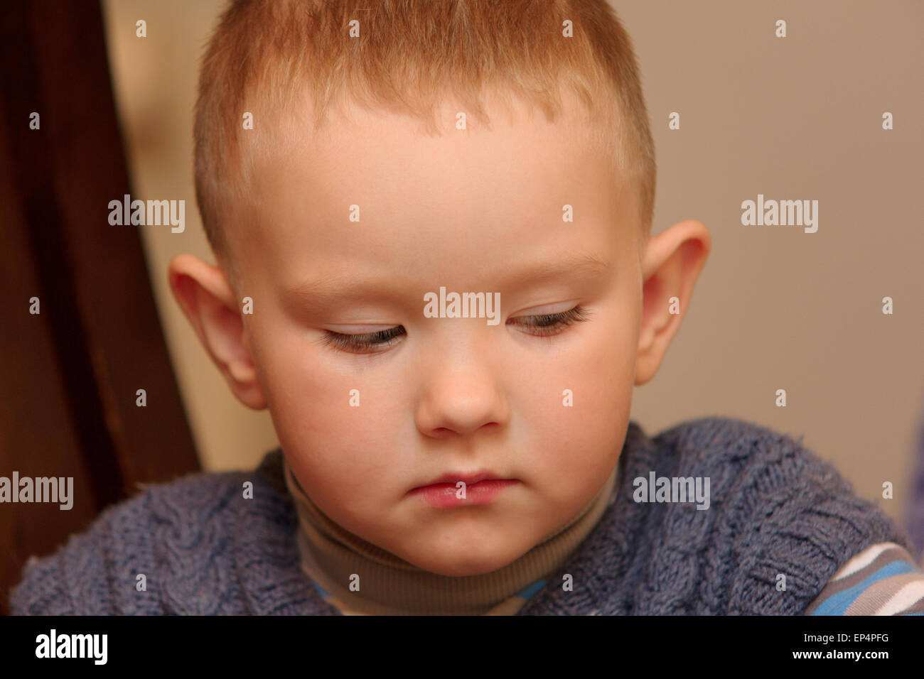 der kleine Junge sitzt auf einem Stuhl und leider schaut Stockfoto