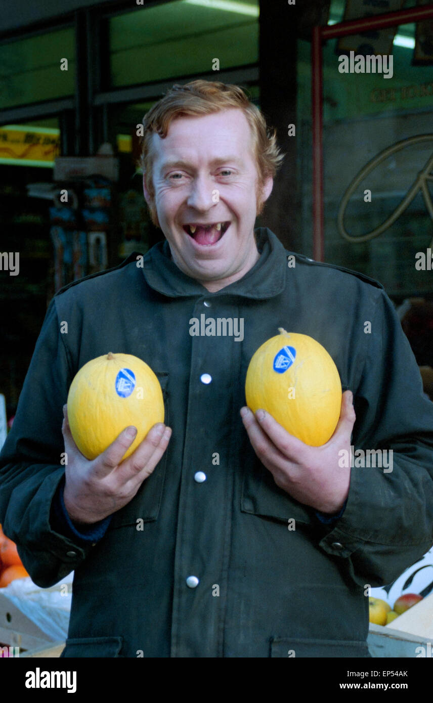 ein Lächeln auf den Lippen zahnlose Gemüsehändler hält zwei Grapefruit außerhalb seiner Shops in Southsea England in den 1990er Jahren Stockfoto