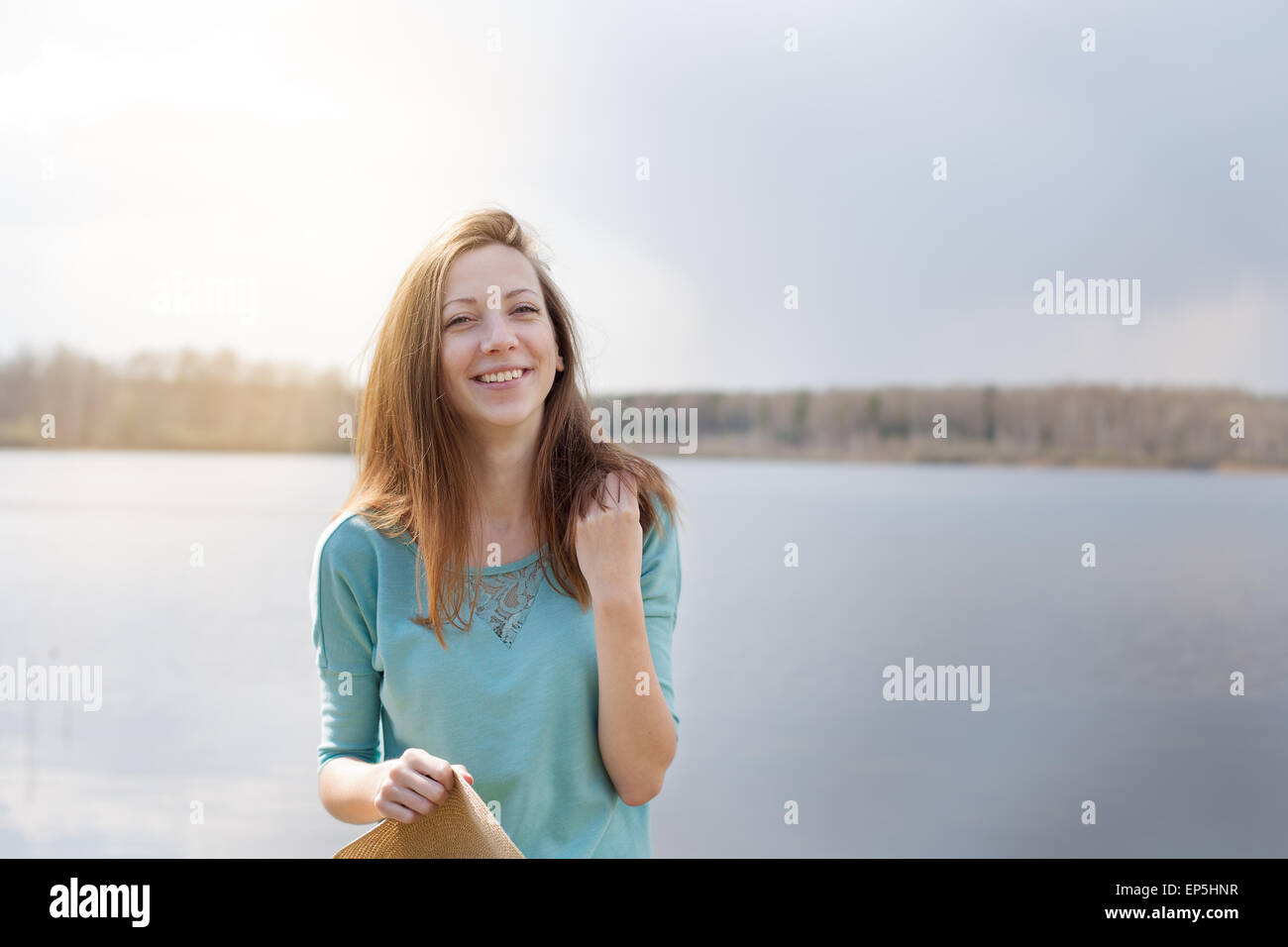 Lächelnd und glücklich Mädchen mit Hut in der Hand auf dem See Stockfoto