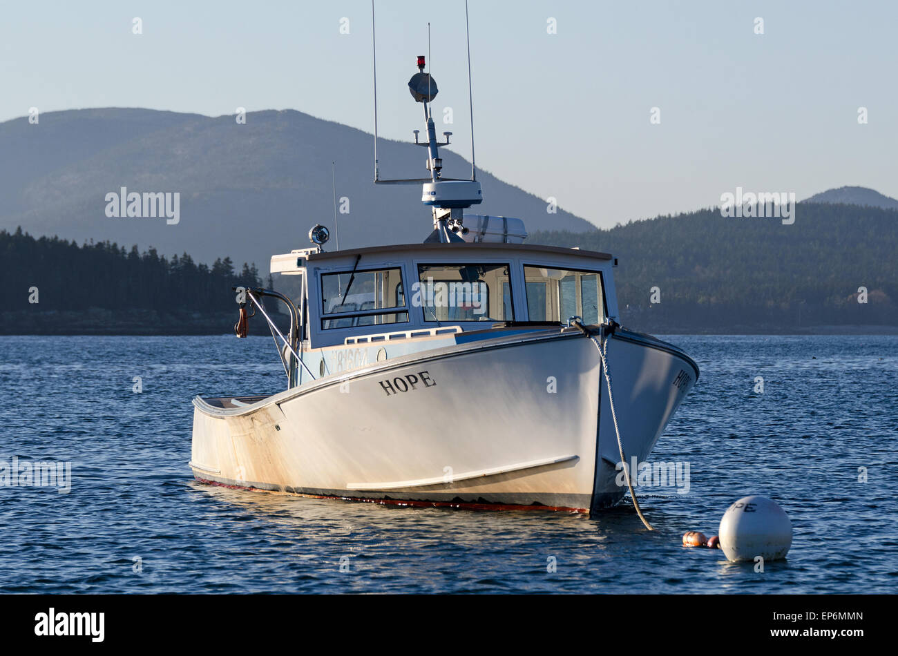 'Hope', ein Hummer-Boot im Hafen von Islesford, Maine, mit den Bergen des Acadia National Park in der Ferne festgemacht. Stockfoto