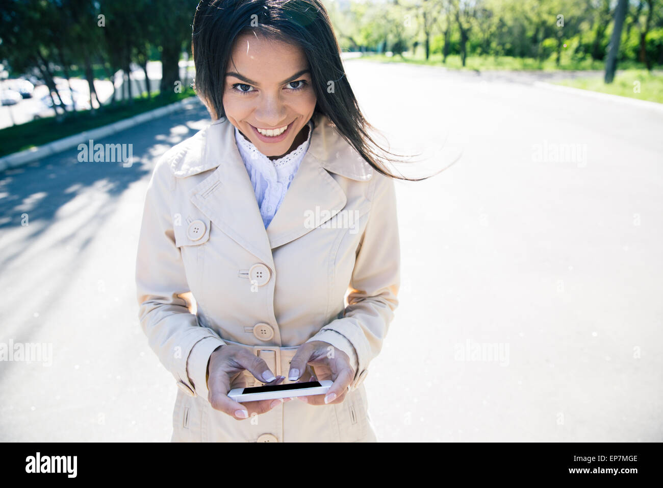 Glückliche Frau zu Fuß und mit Smartphone im Freien. Blick in die Kamera Stockfoto
