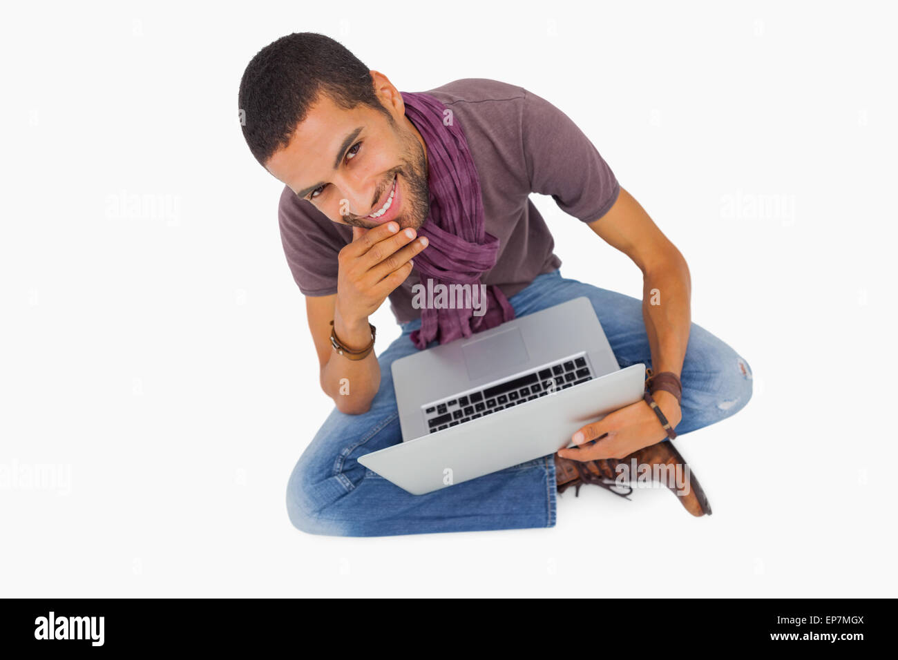 Nachdenklicher Mann sitzen auf Boden mit Laptop und lächelt in die Kamera Stockfoto