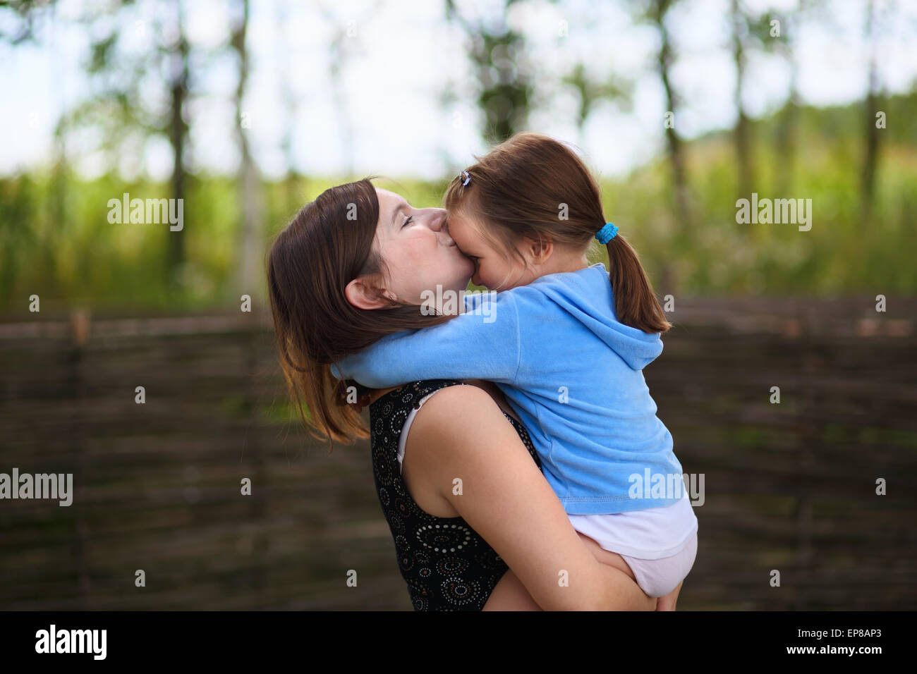 Die Liebe einer Mutter. Mama hält kleine Tochter in die Arme und küßt sie auf die Stirn. Selektiv auf die Gesichter der Modelle. Stockfoto