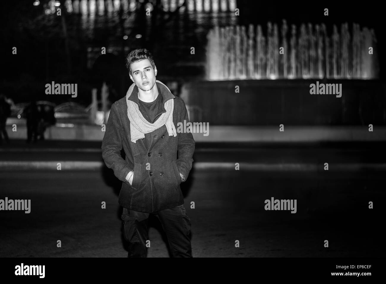 Junger Mann draußen sitzen neben großen Brunnen mit zuversichtlich Ausdruck Stockfoto