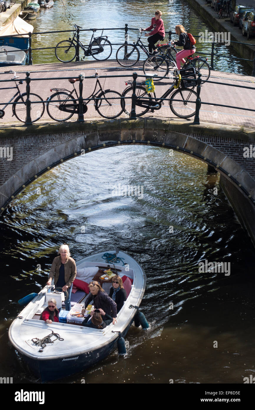 Amsterdam Reguliersgracht Kanal mit einem kleinen Boot und Touristen auf Miet-Fahrräder, die Schwierigkeiten haben, den steilen Brücke fahren. Stockfoto