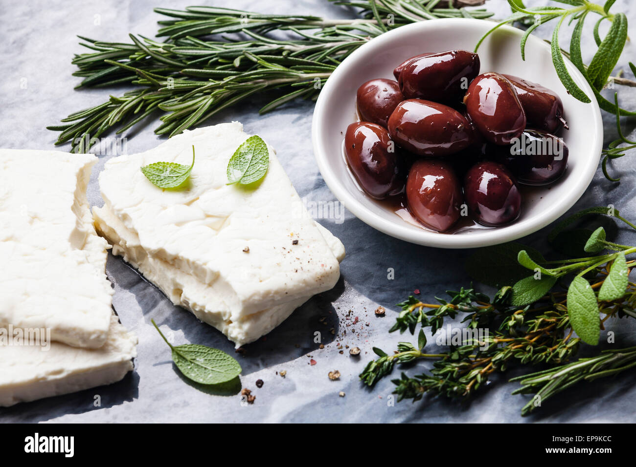 Feta-Käse mit Oliven und grünen Kräutern auf grauem Marmor Hintergrund Stockfoto