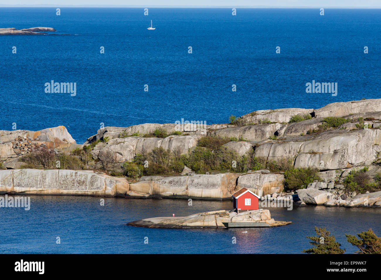 Ziemlich kleine rote Hütte auf einer kleinen Insel mit einem Segelboot in der Ferne Stockfoto