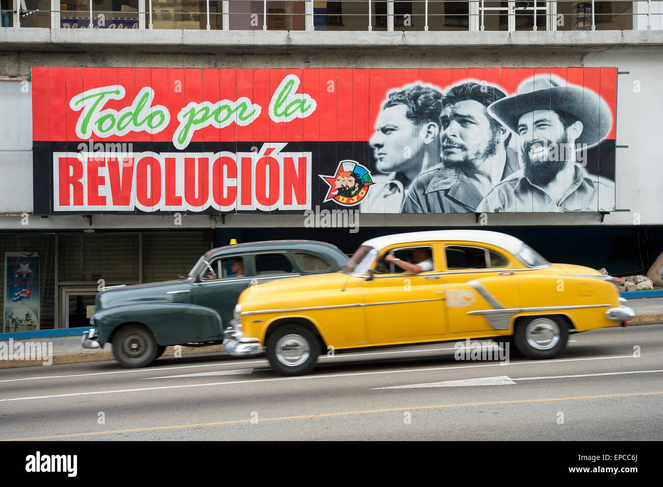 Havanna, Kuba - ca. Juni 2011: American Vintage taxi Autos Pass unter Plakatwand, die Förderung der kommunistischen Propaganda in der La Rampa Stockfoto