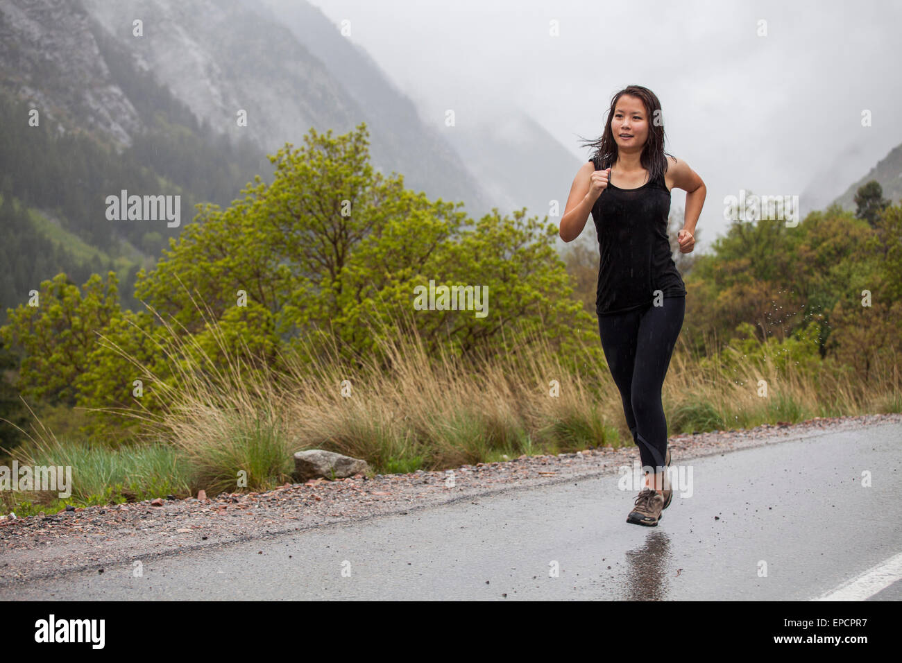 asiatische Frau laufen im Regen unterwegs in Bergen Stockfoto