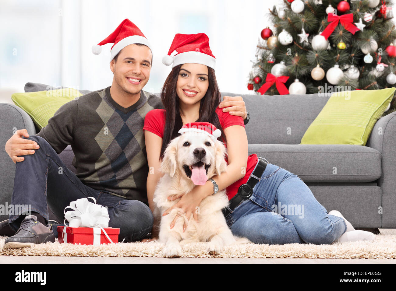 Junges Paar feiert Weihnachten mit ihrem Hund auf dem Boden neben einem modernen Sofa zu Hause sitzend Stockfoto