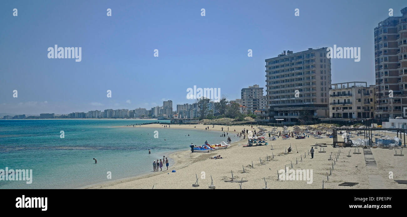 Ferienwohnungen und Hotels am Strand von Varosha Famagusta in der Ferne aufgegeben, während Touristen am nahe gelegenen Strand entspannen. Stockfoto