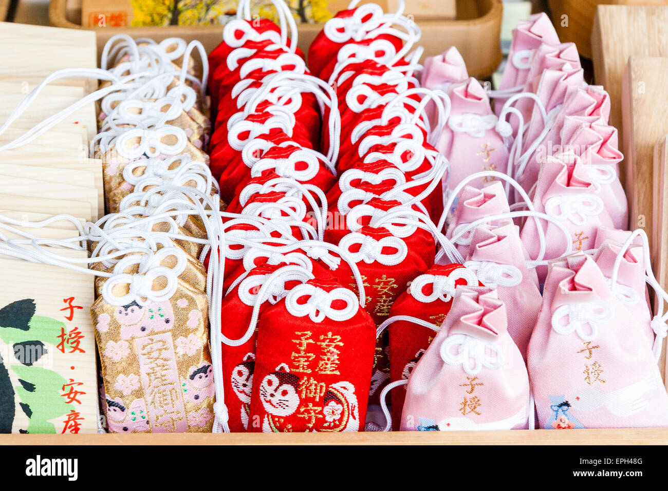 Reihen von roten und rosa omamori Glück Reize mit weißen Krawatten Kordeln, in Reihen auf der Theke eines schintoistischen Schrein in Japan gestapelt. Stockfoto