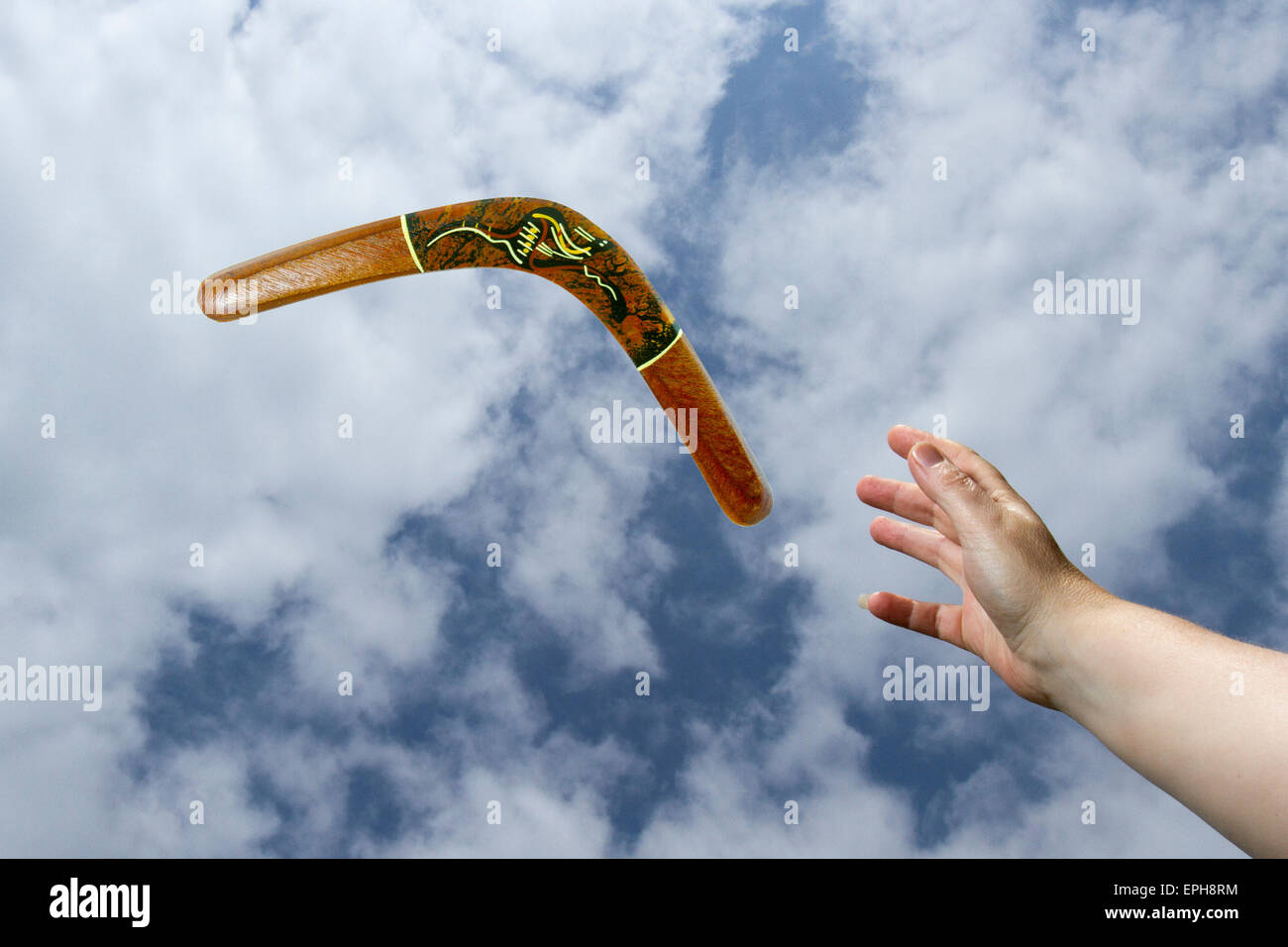 Hand eine bemalte, hölzerne Bumerang Luft mit blauem Himmel und Wolken Hintergrund zu fangen. Stockfoto