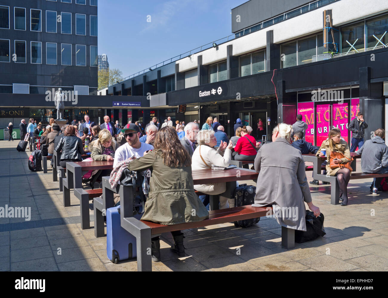 Reisende warten bei Sonnenschein im Sitzbereich außerhalb beschäftigt Euston Station, (derzeit renoviert), central London UK Stockfoto