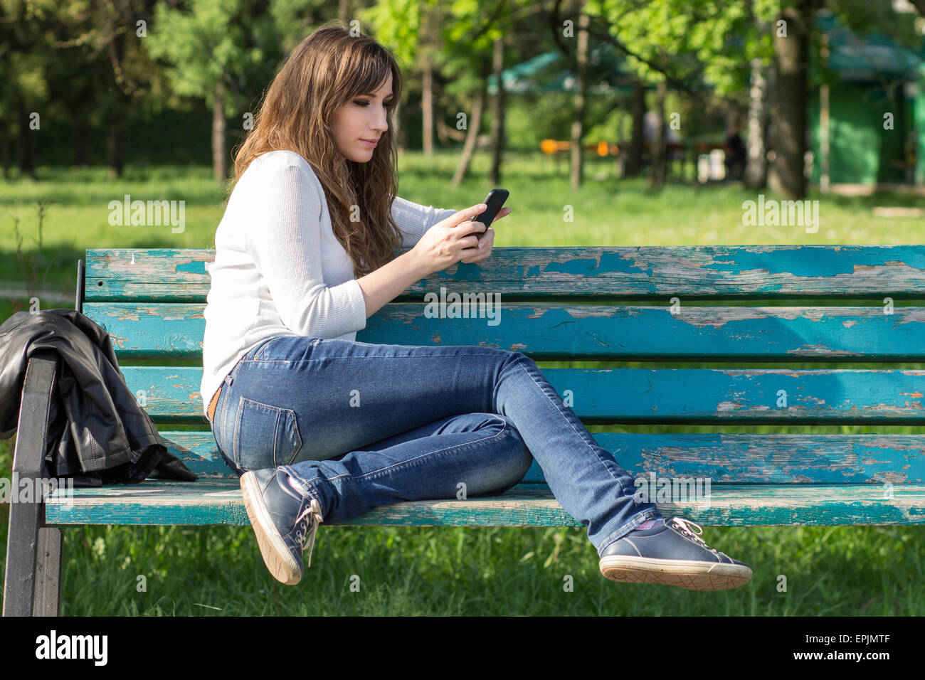 Hübsche junge Frau mit Smartphone sitzen auf Bank im Park am Sommertag. Mädchen auf der Bank ausruhen Stockfoto