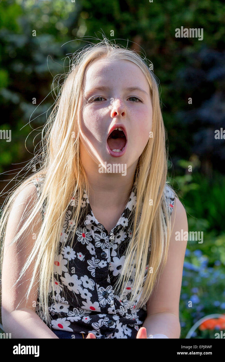 8 Jahre alte Blondine sitzt im Garten schreien beim Fotografen Stockfoto