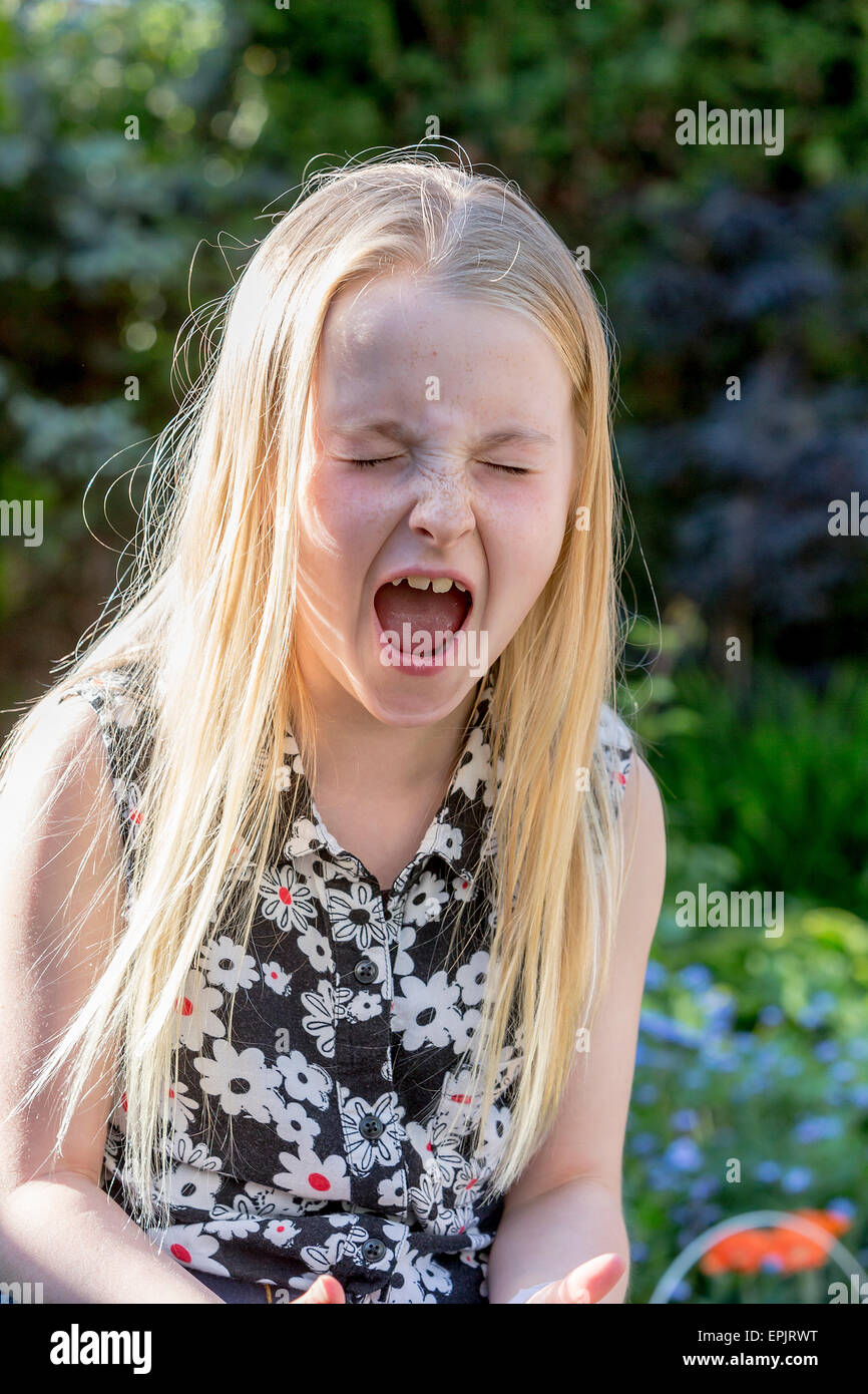 8 Jahre alte Blondine sitzt in einem Garten laut schreien Stockfoto