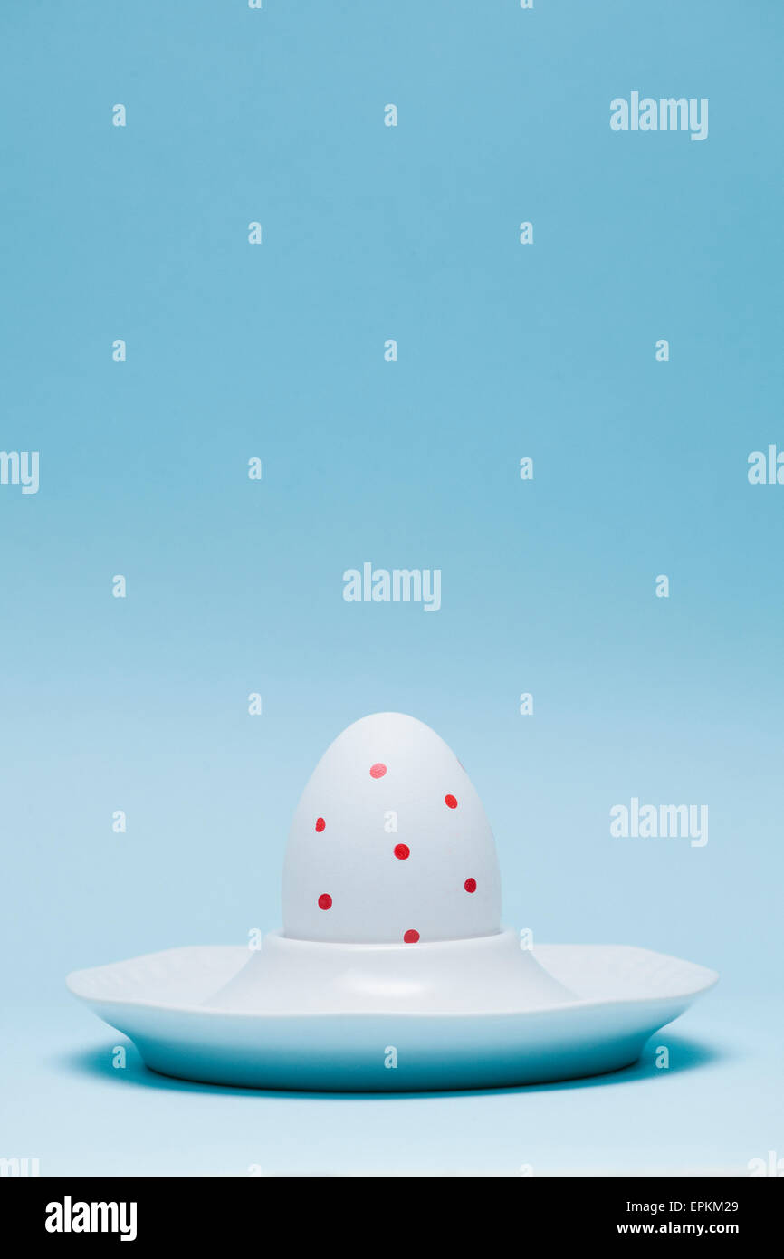 Ei mit roten Punkten in Eierbecher vor hellblauem Hintergrund gemalt Stockfoto