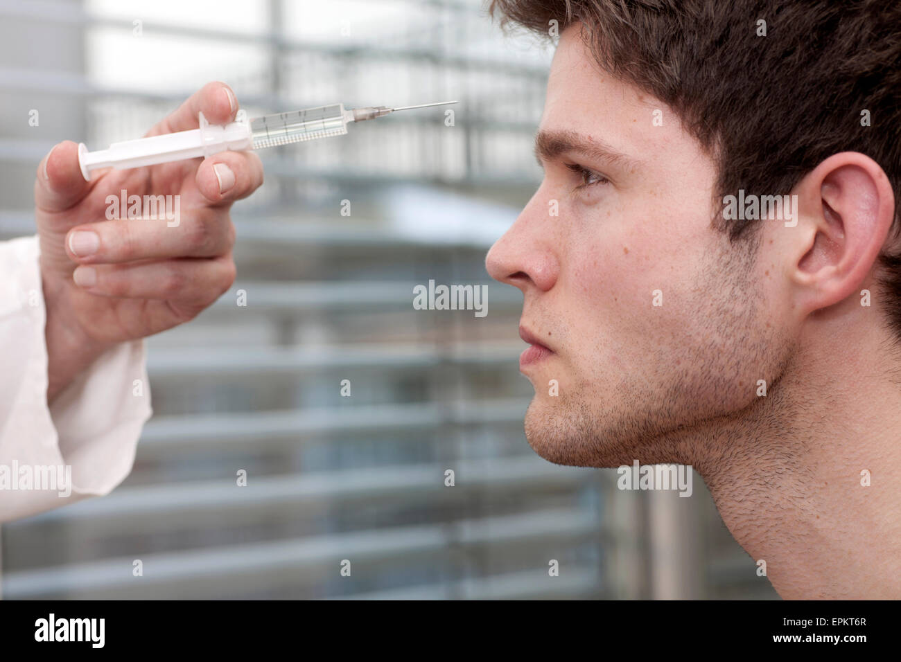 Arzt-Holding-Spritze im Gesicht eines jungen Mannes Stockfoto