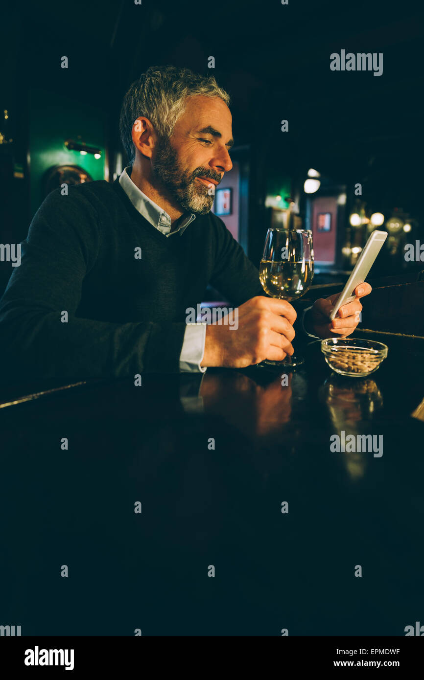 Lächelnder Mann sitzen an der Theke einer Kneipe mit smartphone Stockfoto