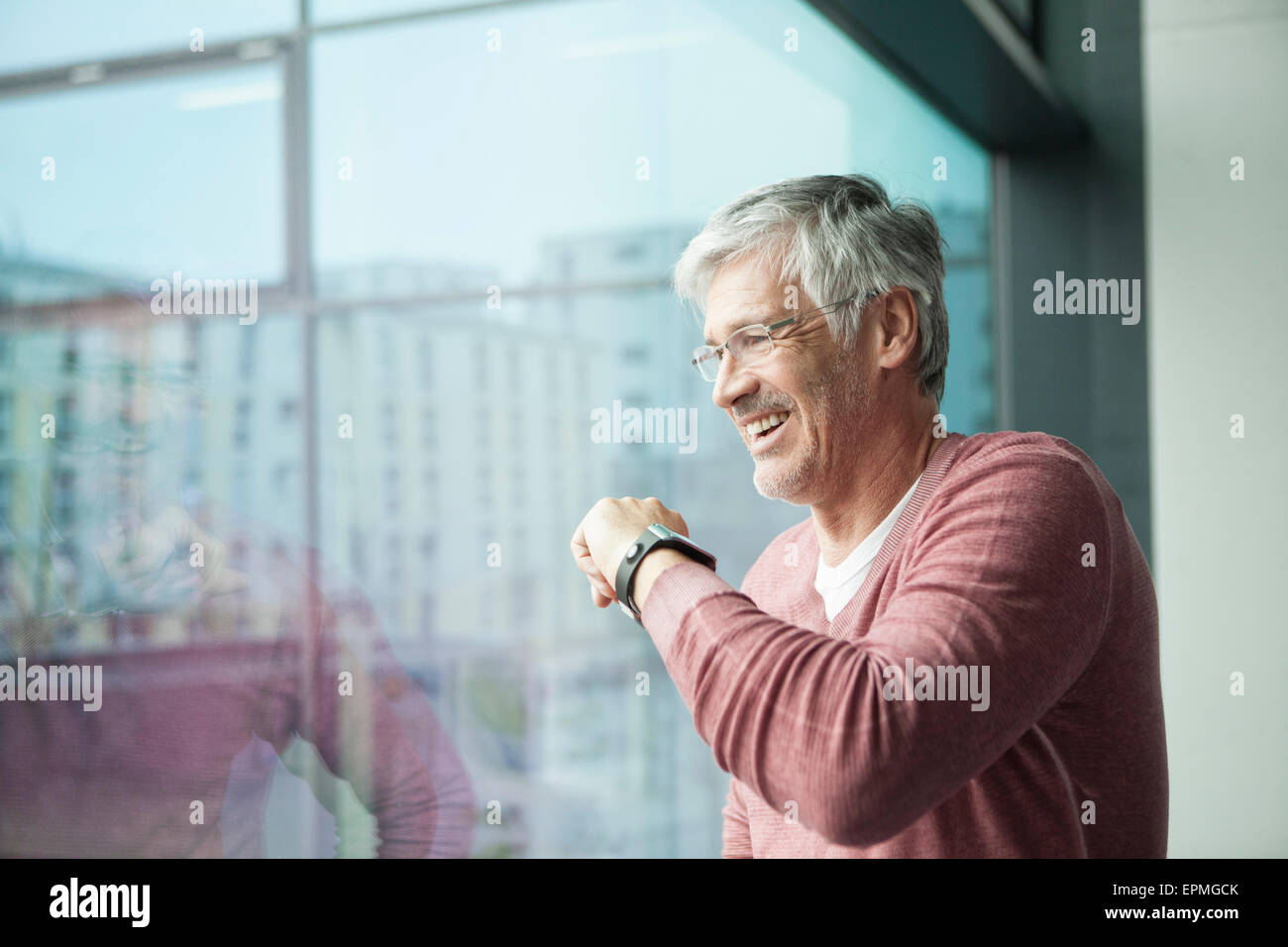 Lächelnder Mann mit Smartwatch Blick durch Fenster Stockfoto