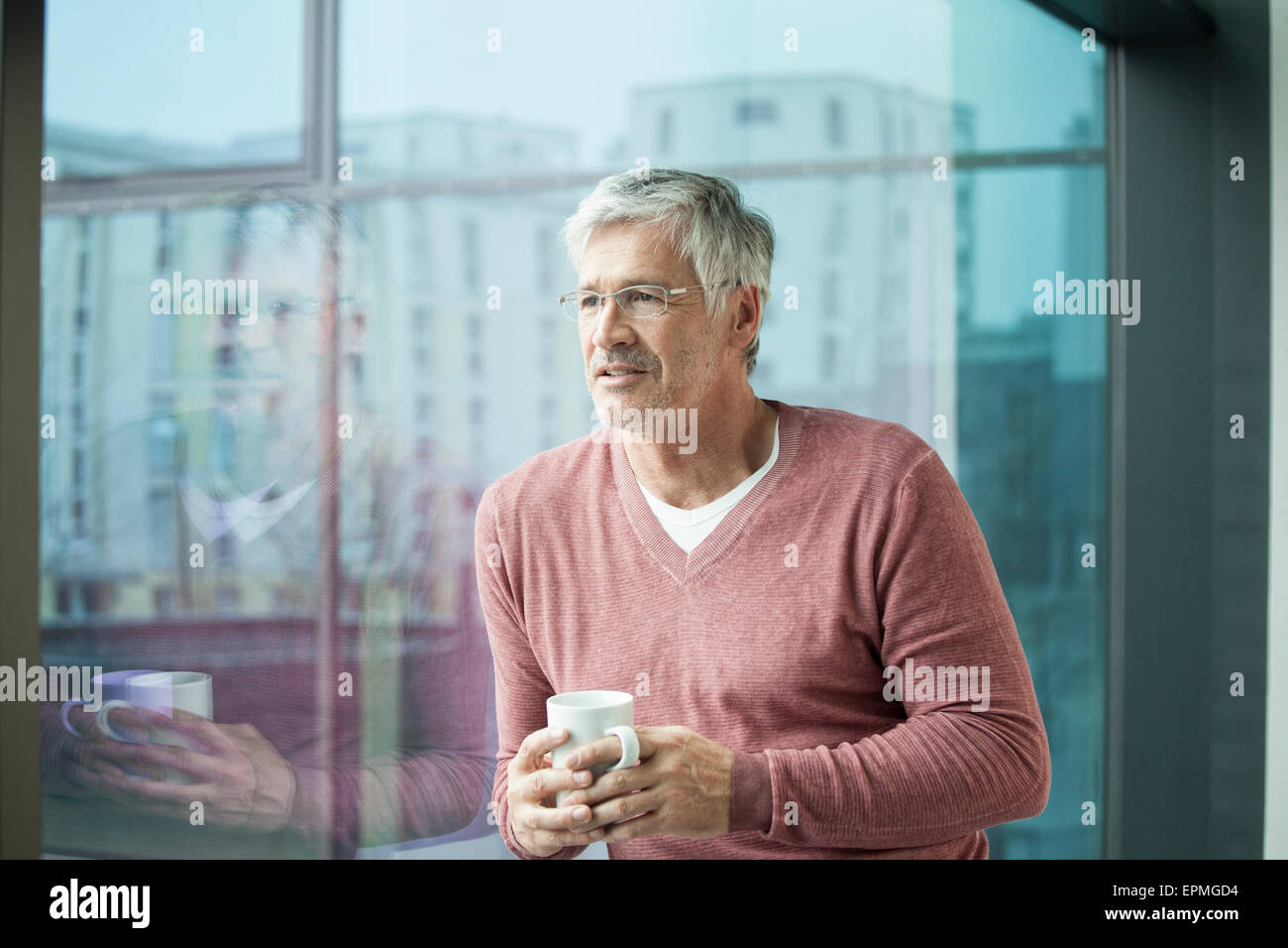 Porträt des Mannes mit Kaffeetasse Blick durch Fenster Stockfoto