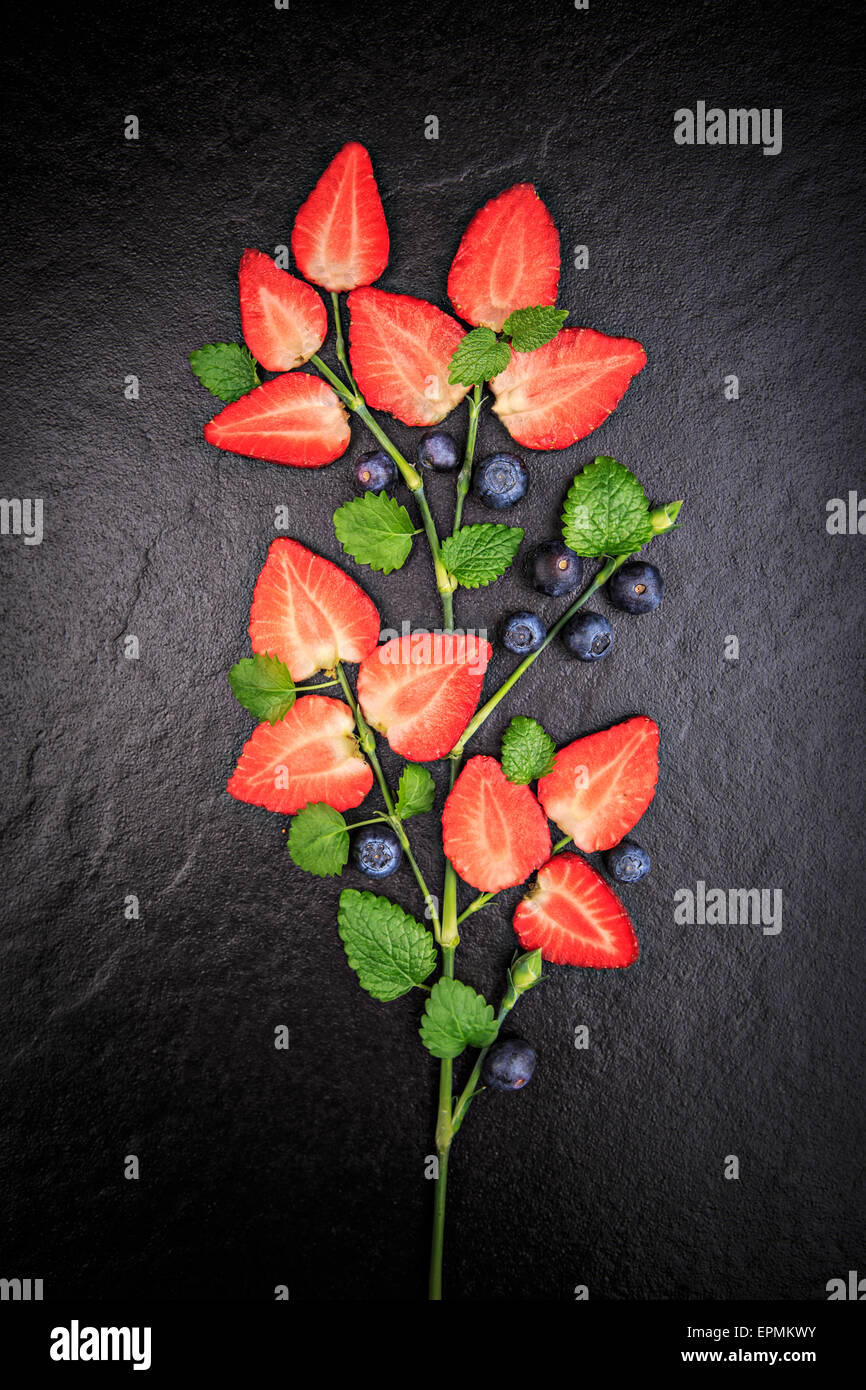 Symbolischen Blume geformt von Melissa, geschnittene Erdbeeren und Heidelbeeren auf Schiefer Stockfoto