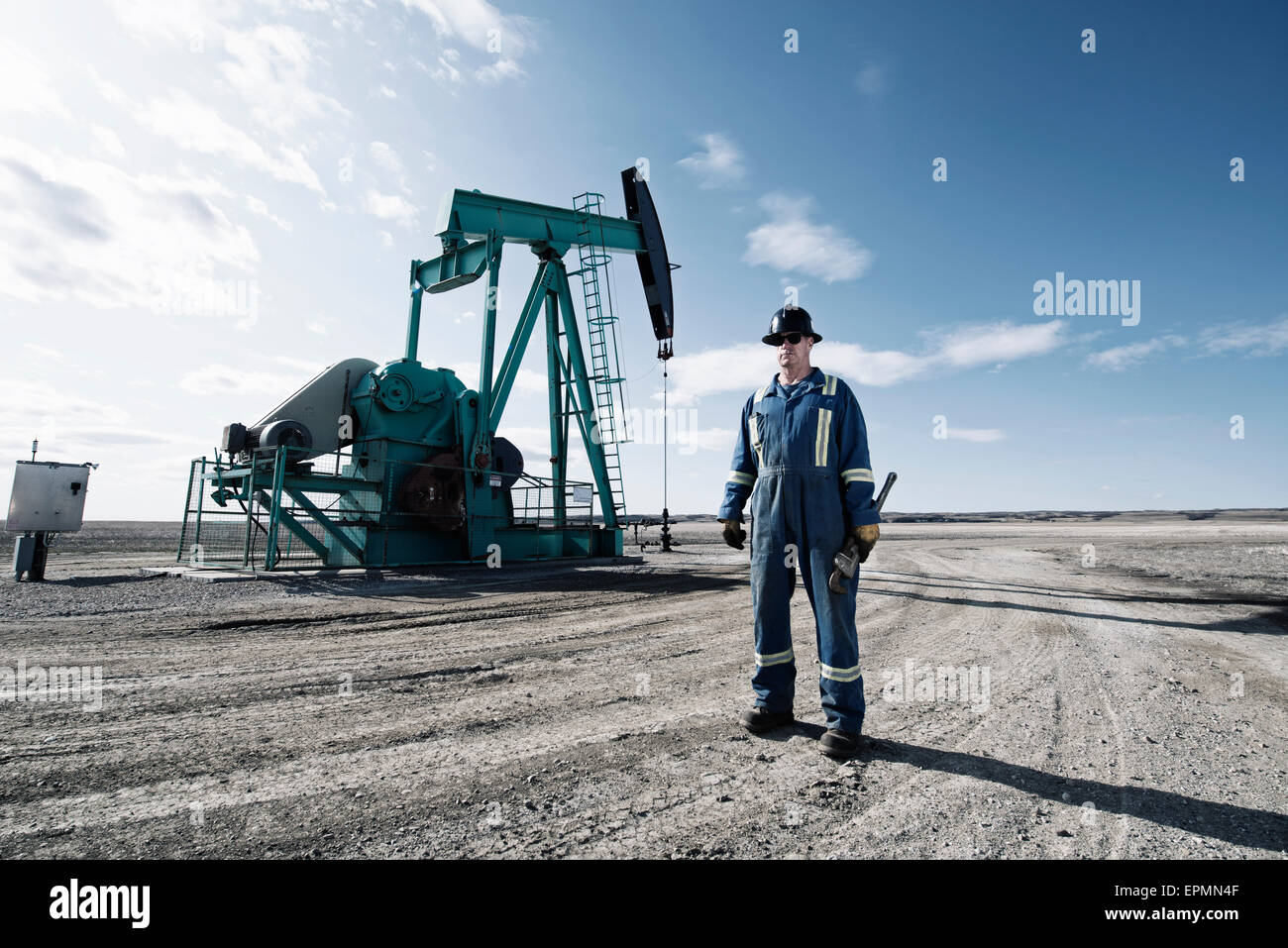 Ein Mann im Overall und einen Schutzhelm mit einem großen Schraubenschlüssel arbeiten auf einer Öl-Extraktion-Website. Stockfoto