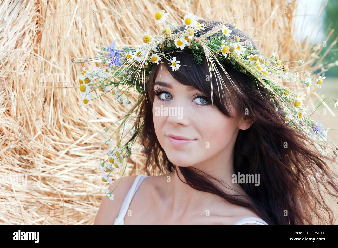 Sommerportrait eines schönen Dorfmädchen in einem Kranz auf einem Hintergrund von Heu.Foto getönt hellgelb, um Sommeratmosphäre zu übertragen Stockfoto