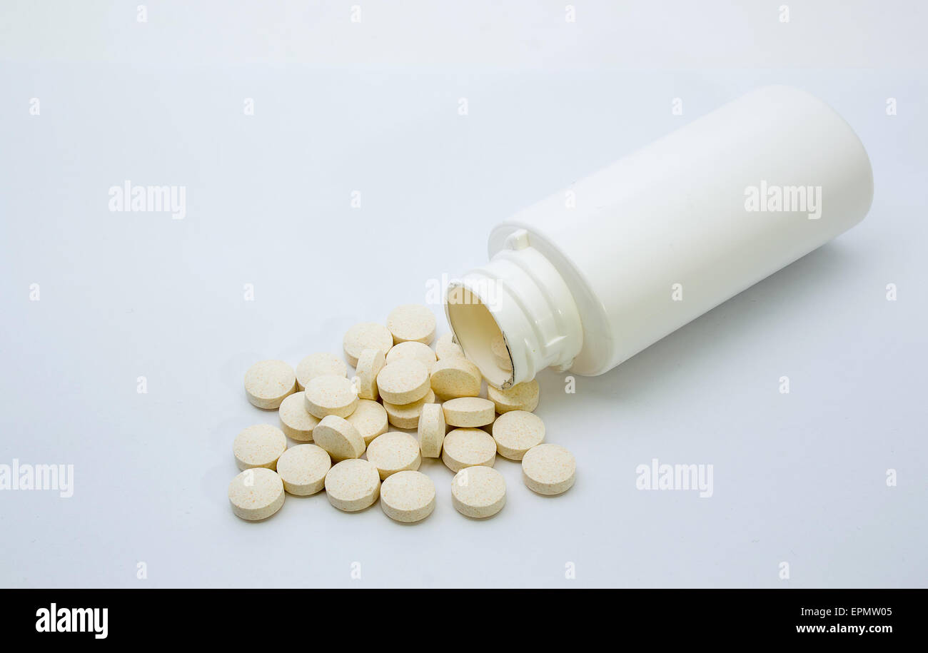 Vitamintabletten aus einer weißen Flasche geschüttet und auf einem weißen Hintergrund angezeigt Stockfoto