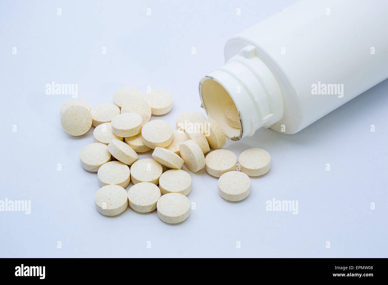 Vitamintabletten aus einer weißen Flasche geschüttet und auf einem weißen Hintergrund angezeigt Stockfoto