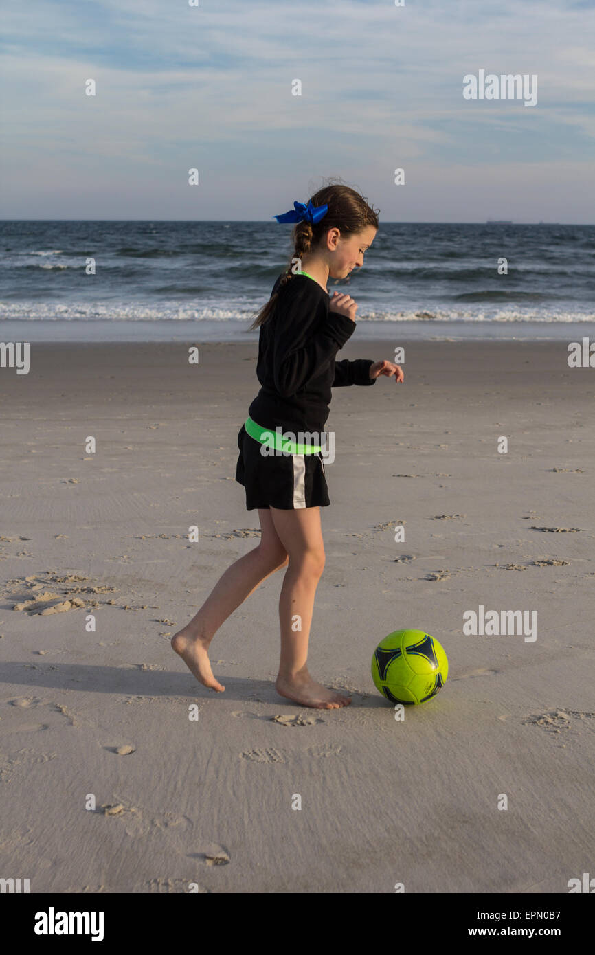 Ein Zehn Jahres altes Mädchen spielt mit einem Fußball am Meer entlang in Long Beach, New York. Sie spielt Fußball auf ihrer Schule-Team. Stockfoto